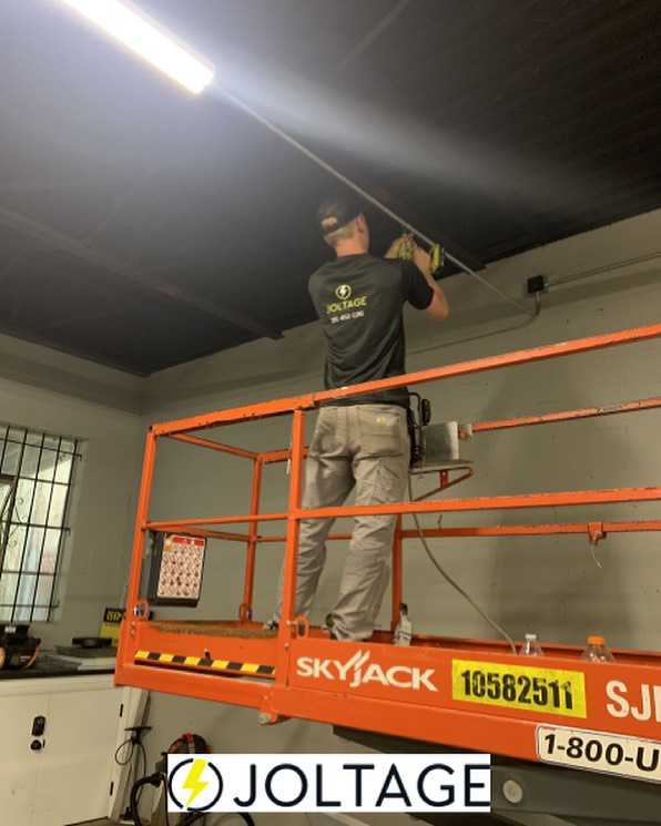 An electrician installing overhead lighting and conduit from a scissor lift for Joltage LLC in Mobile, AL.