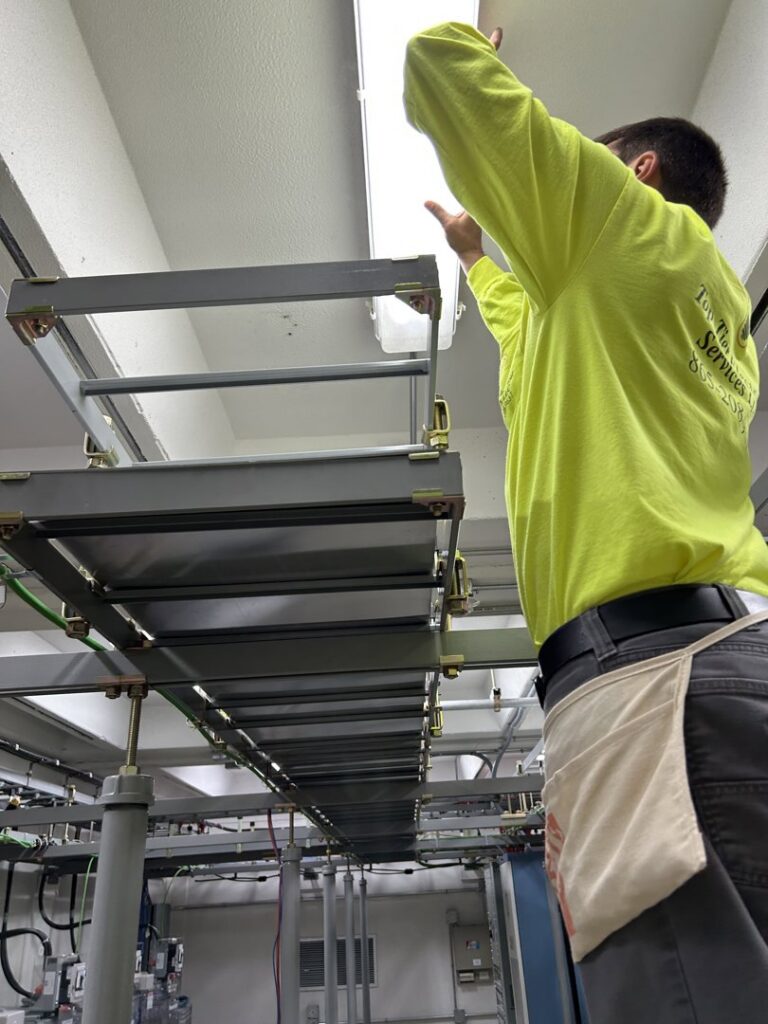 An electrician installing or maintaining overhead lighting and wiring in a commercial space by Top Tier Electrical Services LLC in Knoxville, TN