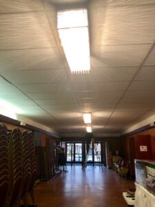 An electrician on a ladder installing overhead lighting in a large hall for Detroit Voltage in Detroit, MI.