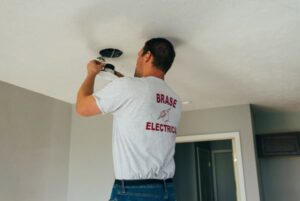An electrician installing a recessed light fixture in a ceiling for Brase Electrical Contracting Corp in Omaha, NE.
