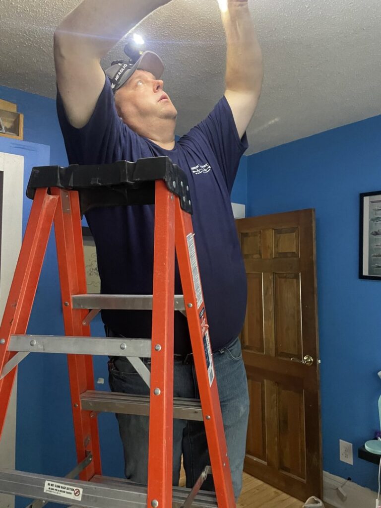 An electrician on a ladder installing a recessed light fixture in a ceiling for LeBrun Electric, Heating & Cooling in Brooklyn Park, MN.
