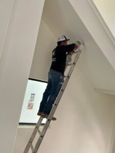 An electrician from Shark Electric installing a recessed light fixture in a sloped ceiling in Houston, TX.