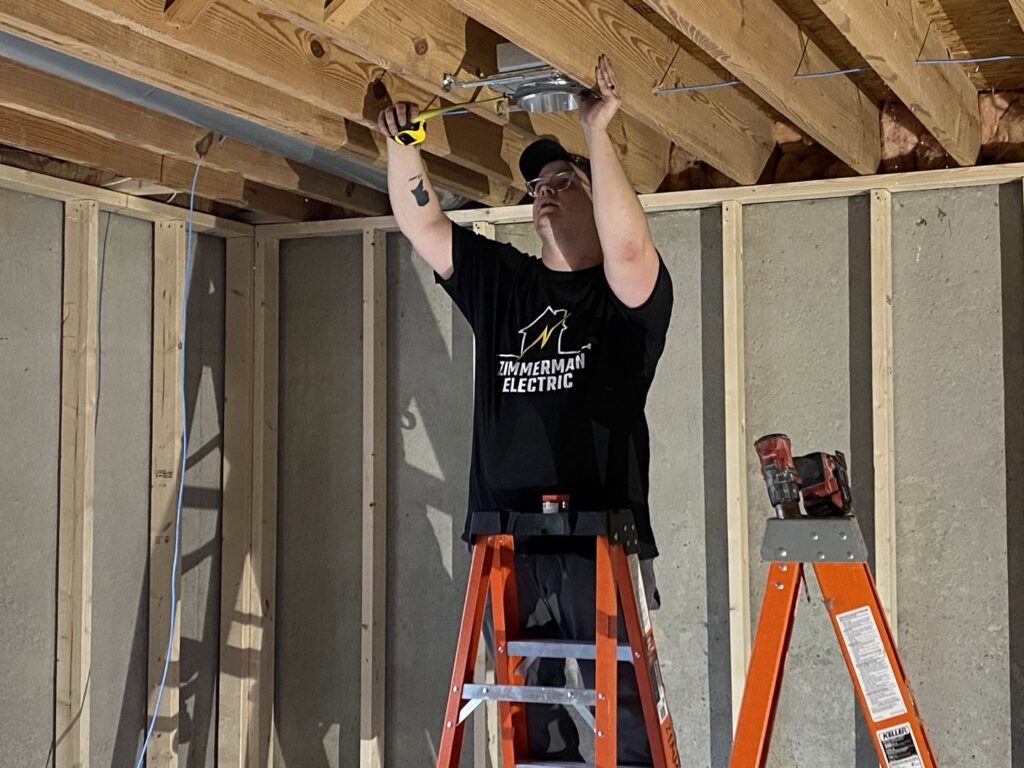 An electrician from Zimmerman Electric Indy installing a recessed light fixture in a ceiling in Indianapolis, IN
