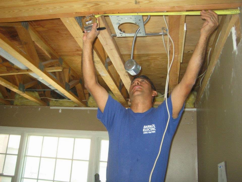 An electrician from Barrios Electric LLC measuring for recessed lighting installation in a ceiling in Norwalk, CT.