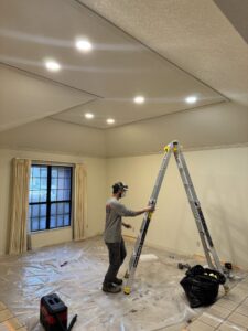An electrician on a ladder installing recessed lighting in a room for Electrical Power Source in Fresno, CA.