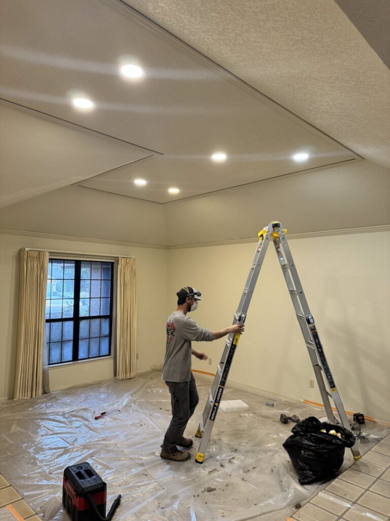 An electrician on a ladder installing recessed lighting in a room for Electrical Power Source in Fresno, CA.