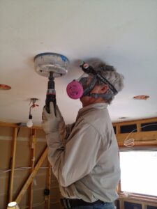 An electrician from Swartz Electric installing recessed lighting in a ceiling, with exposed wiring visible in Colorado Springs, CO.