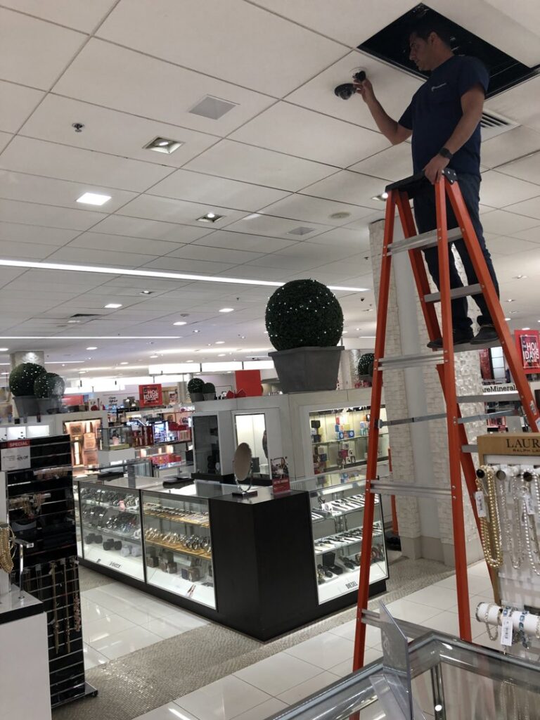 An electrician on a ladder installing a security camera in a commercial retail store, performed by PTech Installs in Columbus, GA.