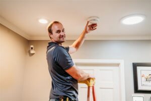 An electrician from Arnold Electrical Repair & Installation on a ladder installing a smoke detector in a home in Chicago, IL.