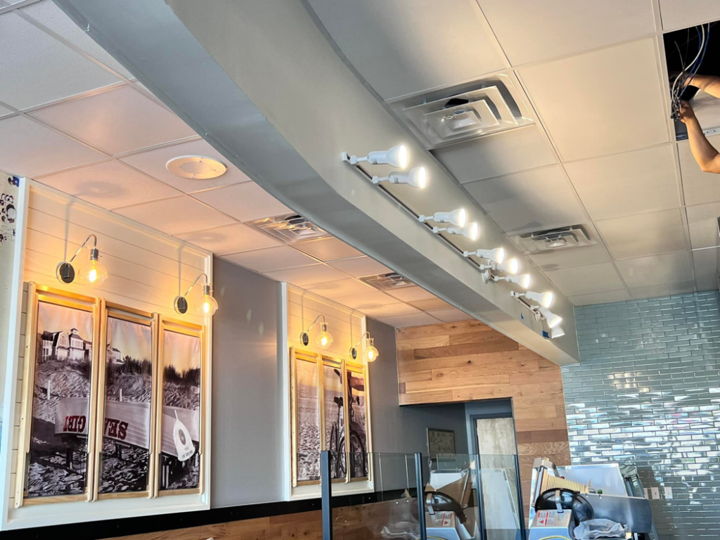 An electrician installing modern track lighting and wall sconces in a commercial space by Solution Electric in Houston, TX.