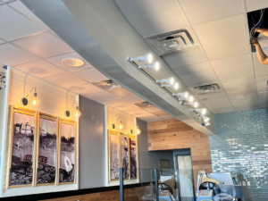 An electrician installing modern track lighting and wall sconces in a commercial space by Solution Electric in Houston, TX.