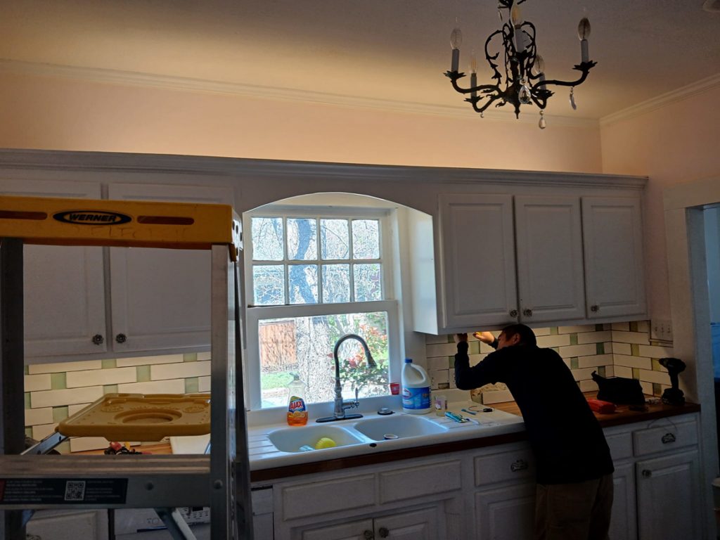 An electrician from Jesano Electric in Fort Worth, TX, installing or repairing wiring under kitchen cabinets.
