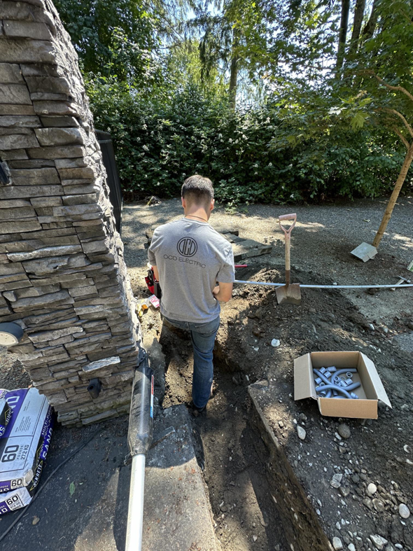 An electrician from OCD Electric installing underground electrical conduit in a trench in Spokane, WA.