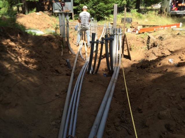 An electrician installing underground electrical conduits in a trench for Johnsen Electric Inc in Springfield, OR.