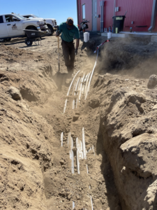 An electrician from On Point Electrical Services installing underground electrical conduits in a trench in Williston, ND.