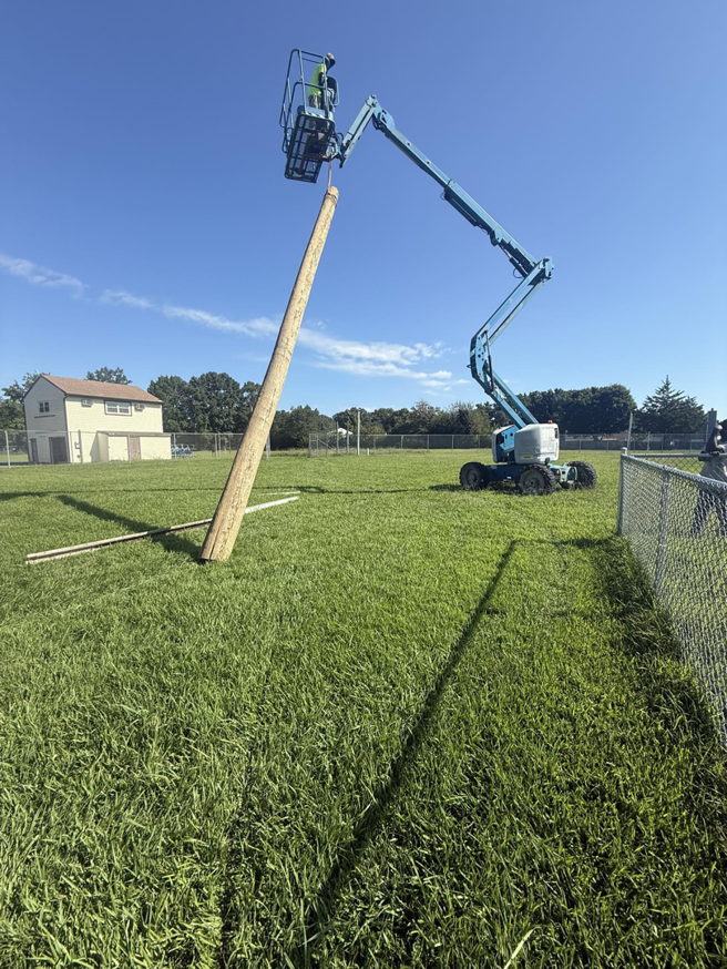 An electrician from Relay Electric, LLC using a boom lift to install a tall wooden utility pole in Suffolk, VA.