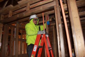 An electrician on a ladder installing wiring and conduit in a framed building under construction by CM Armitage Electrical Contracting Inc in Rochester, NY.
