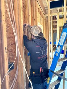 An electrician installing wiring inside a framed wall at a job site for Justin Benevage Electrical, LLC in Lake Charles, LA