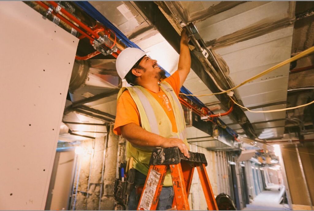 An electrician installing electrical wiring and conduit in a commercial ceiling for Bay Electric Co. in Newport News, VA.
