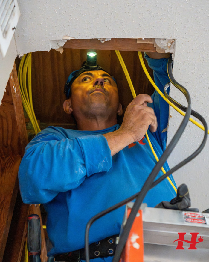 An electrician from Powered By H installing electrical wiring in a ceiling space in Houston, TX.