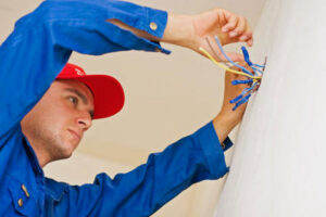 An electrician in a blue uniform and red cap installing new wiring into a wall, performed by Rylix Electric in Cincinnati, OH.