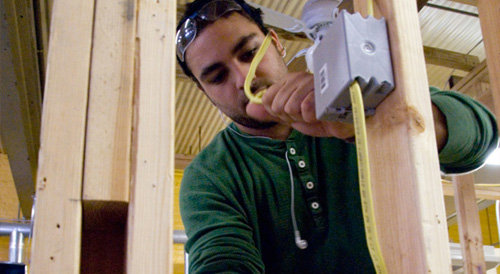 An electrician in safety glasses installing new electrical wiring within a wall frame, a service from Your Gilbert Electrician in Gilbert, AZ.