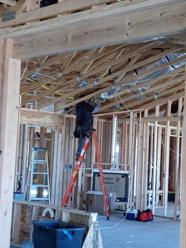An electrician installing electrical wiring in the ceiling of a new construction project for The Specialist Electrical Contractor in Albuquerque, NM.