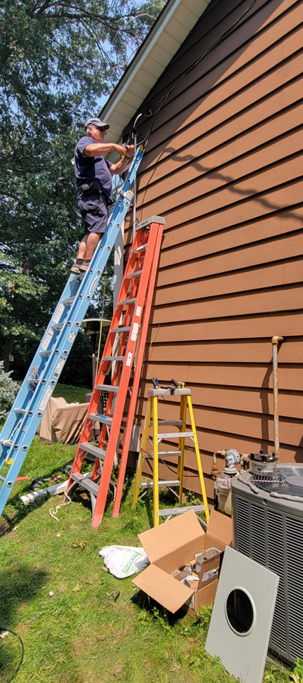 An electrician on a ladder performing outdoor wiring work on a house for John Kivel Electric, LLC in Woodbury, MN.