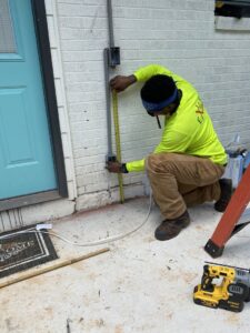 An electrician from High Electrical measuring for conduit installation on the exterior of a house in Atlanta, GA.