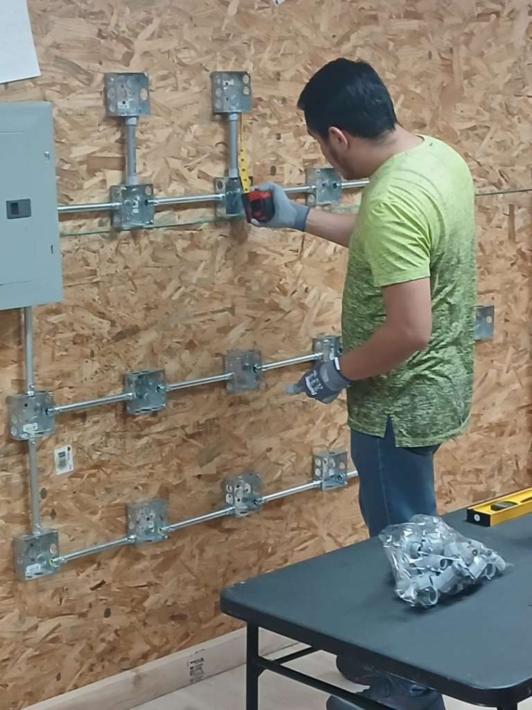 An electrician measuring electrical conduit and box installation on a wooden wall at Millan Electric Service llc in Las Vegas, NV