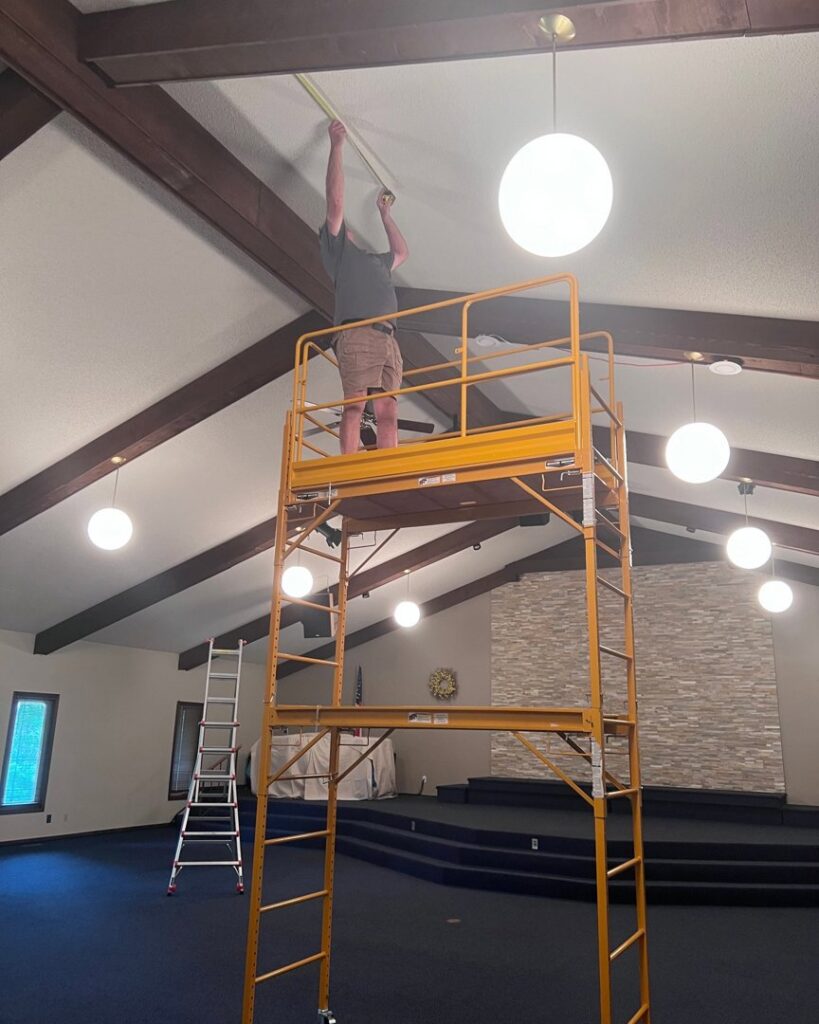 An electrician from Coffin Electric measuring for a lighting installation on scaffolding in Grimes, IA.