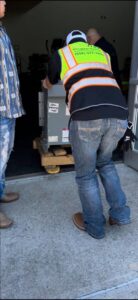An electrician from Brighton Electrical Services moving a large electrical transformer on a dolly in Laredo, TX.