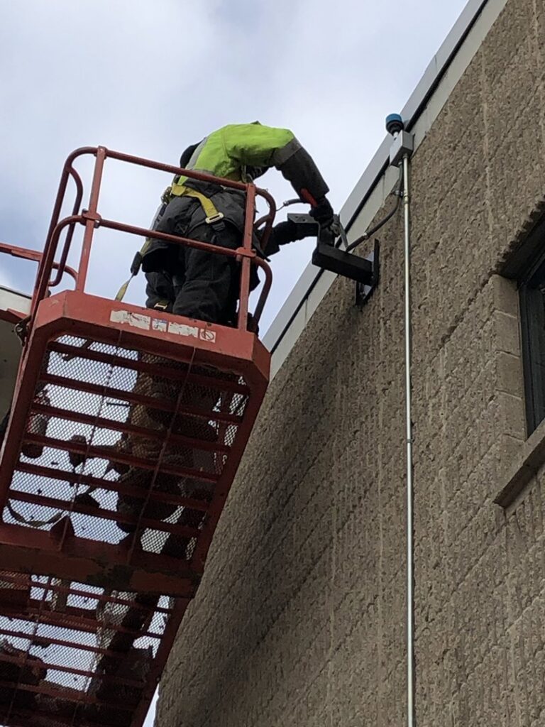 An electrician on a boom lift working on an exterior wall, performing installation or repair for RHS Electrical Services in Westerville, OH.