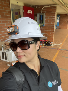 An electrician wearing a hard hat and company shirt on a job site with an electrical panel in the background, by Mcdaniel Electric, LLC in Waipahu, HI.