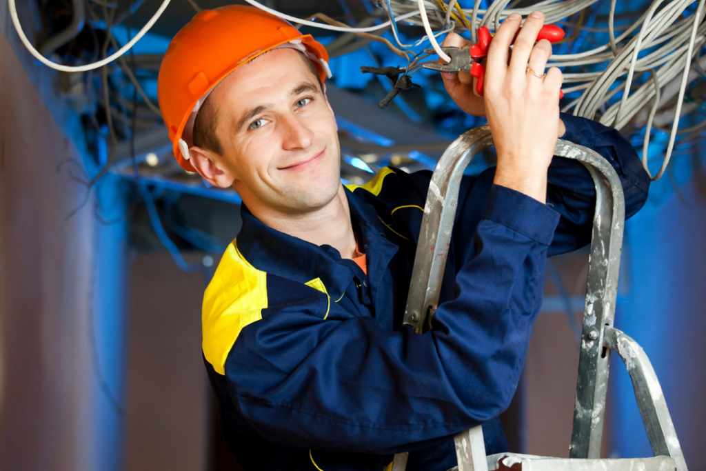 A smiling electrician from EMS Electric of Monroe LLC on a ladder working with wires in Monroe, LA.