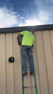 An electrician on a ladder working on an outdoor electrical box for Polsley Electric Company in Omaha, NE