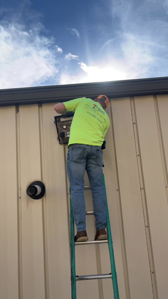 An electrician on a ladder working on an outdoor electrical box for Polsley Electric Company in Omaha, NE