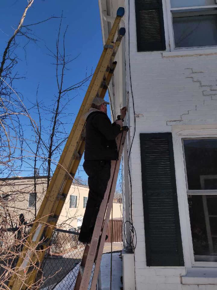 An electrician from Lindquist Electric on a ladder performing work on the exterior of a house in Upton, MA.