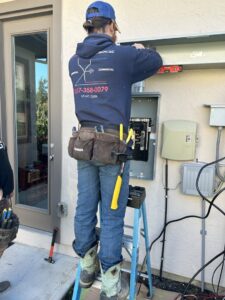 An electrician on a ladder working on an outdoor electrical panel for Justin Benevage Electrical, LLC in Lake Charles, LA