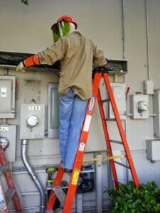 An electrician on a ladder performing work on outdoor electrical boxes and meters for Sterling Wiring Solutions in Pearland, TX.