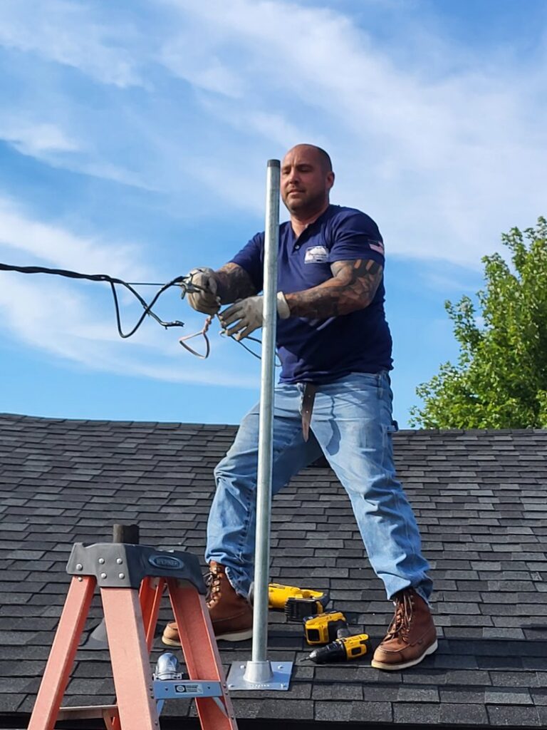 An electrician from National Electric - Lansing on a roof installing an electrical mast in Lansing, MI.