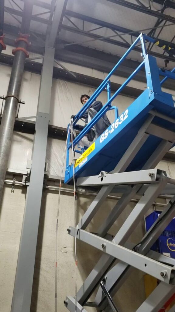 An electrician from Henelect Electrical Contractors on a scissor lift installing overhead wiring in Milford, NJ.