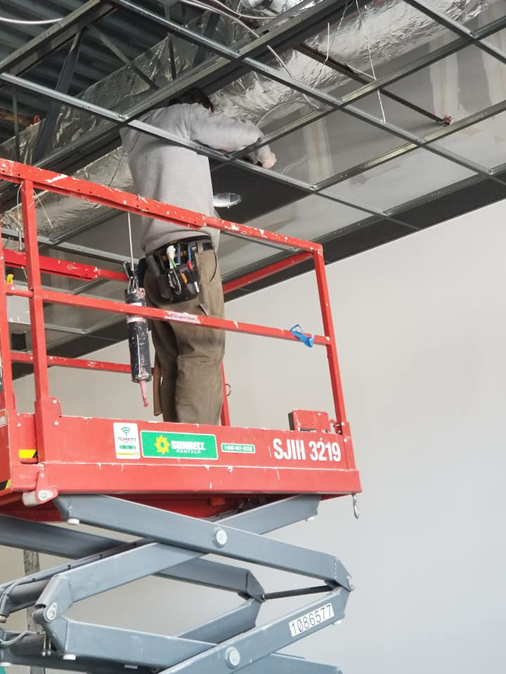 An electrician on a scissor lift installing overhead wiring and conduit for 2 Phase Electric LLC in Barnesville, MN.