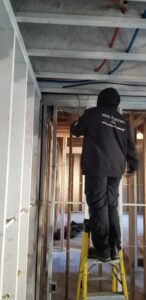 An electrician from Vets Electric Company installing overhead wiring on a ladder in Tacoma, WA