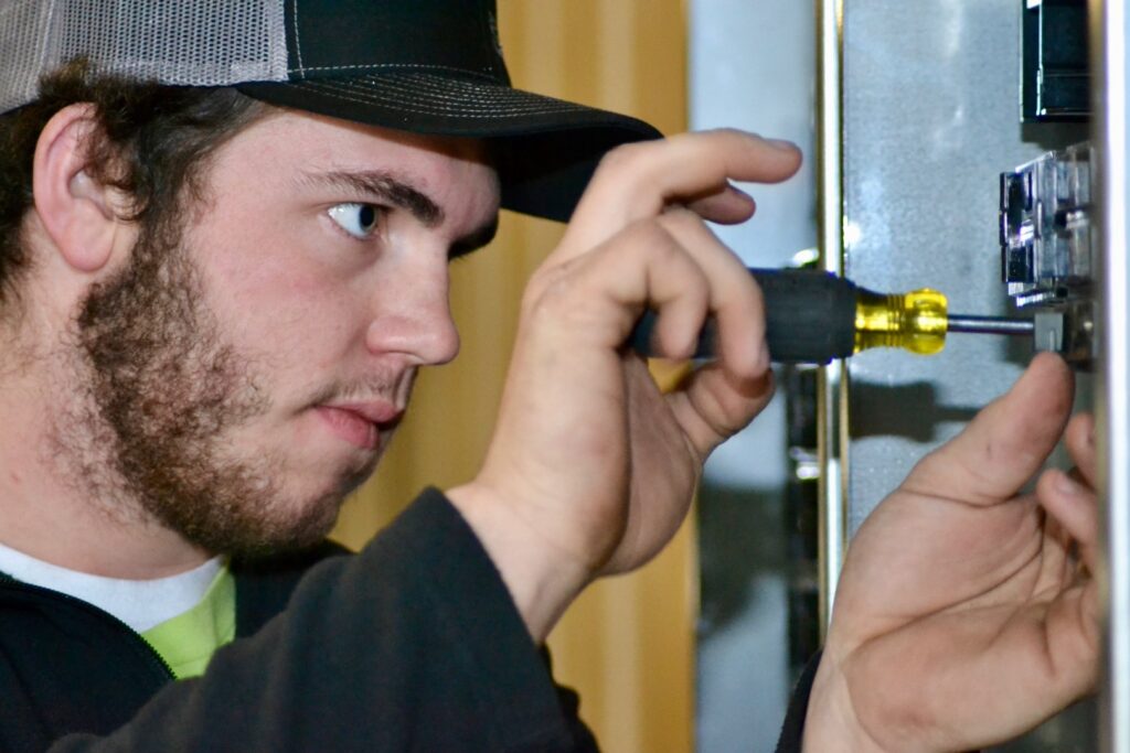 A young electrician performing detailed electrical work with a screwdriver on a panel for Rebco Electric in Lebanon, OH.