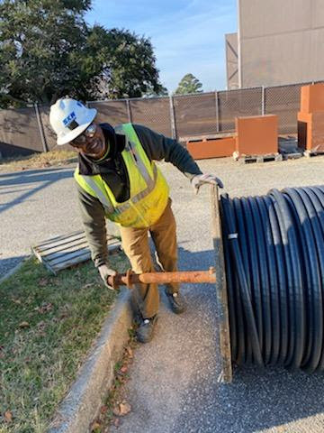 An electrician from Bay Electric Co. pulling a large spool of electrical cable on a job site in Newport News, VA.