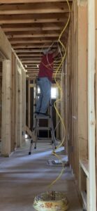 An electrician pulling electrical wire through wall studs during new construction by Outlaw Home Services, LLC in San Antonio, Tx.