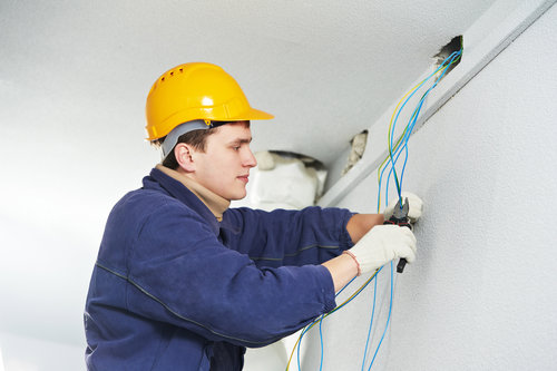 An electrician in a hard hat pulling electrical wires through a wall opening for BrotherlyLove Electric LLC in Houston, TX.