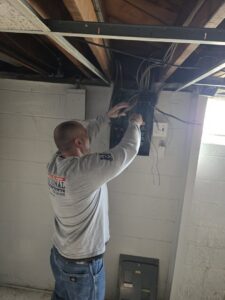 An electrician from National Electric - Lansing repairing a basement electrical panel in Lansing, MI.