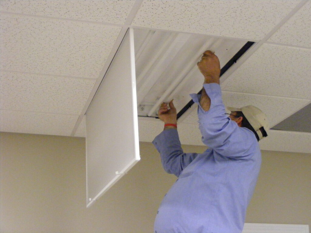 An electrician repairing or installing a fluorescent light fixture in a drop ceiling for Midway Electric in Columbia, MO